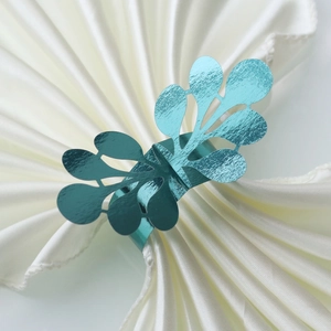 Detailed view of teal glitter napkin ring with a hollow leaf design on white satin
