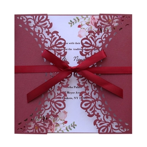 Elegant laser-cut wedding invitation with a red ribbon bow and floral inner card