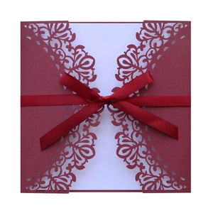 Detailed laser-cut floral patterns on burgundy wedding invitation with a ribbon bow