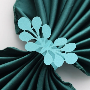 Detail of light blue laser-cut paper napkin ring with hollow leaf design on green fabric