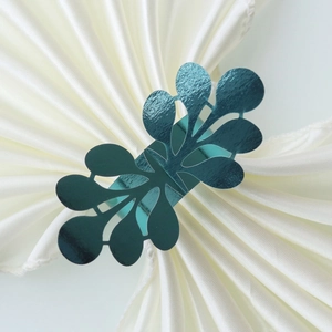 Macro detail of teal glitter paper napkin ring with laser-cut leaf pattern on white satin