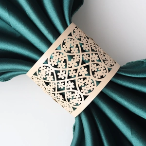 Close-up of laser-cut gold floral paper napkin ring on green satin fabric detail