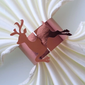 Close-up of rose gold reindeer paper napkin ring on a white cloth for table decor