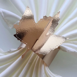 Detail view of a rose gold maple leaf paper napkin ring on white fabric for wedding decor