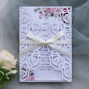 Detail of laser-cut floral wedding invitation with cream ribbon on blue tulle background