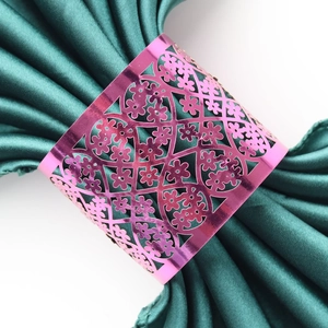 Detail of pink metal napkin ring with hollow floral pattern on a green satin cloth