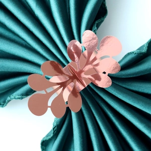 Macro detail of rose gold hollow floral napkin ring on green silk background