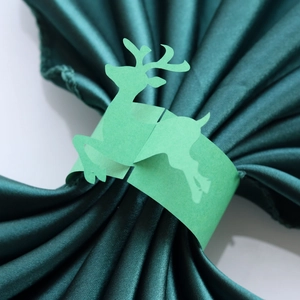 Detail of laser-cut green reindeer paper napkin ring on green silk fabric for Christmas