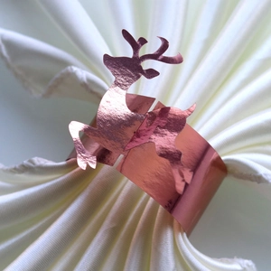 Macro detail of rose gold reindeer napkin ring with reflective mirror finish on white fabric