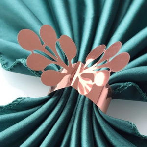Close-up of rose gold napkin ring with hollow leaf design on a green fabric