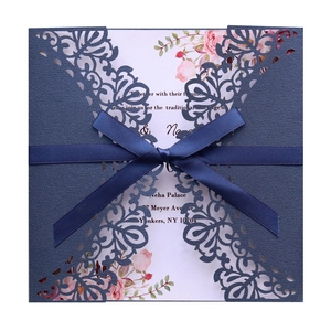 Detail of laser-cut navy blue wedding invitation with silk bow and floral insert
