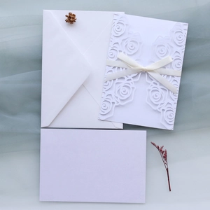 Macro shot of white laser-cut floral invitation with silk ribbon on blue tulle fabric