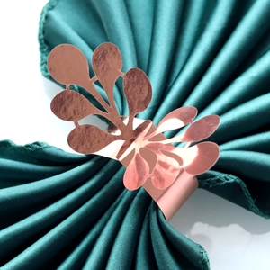 Detailed close-up of rose gold hollow leaf napkin ring on dark green satin fabric