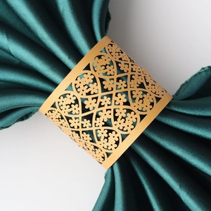 Detail of laser-cut gold napkin ring with intricate floral pattern on green satin