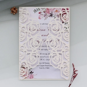 Detail of laser-cut cream wedding invitation featuring rose patterns and floral inner card