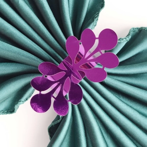 Close-up of purple glitter floral napkin ring on green satin fabric for wedding decor