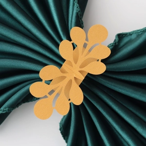 Golden pearl paper napkin ring with hollow leaf design on dark green satin fabric