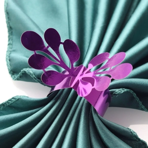 Macro shot of purple butterfly paper napkin ring on a green satin folded napkin