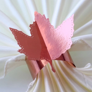Macro detail of rose gold maple leaf napkin ring with hollowed edges on white fabric