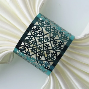 Macro view of teal metal napkin ring with intricate floral lace patterns on white silk
