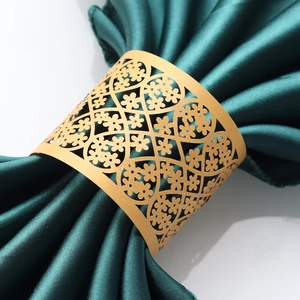 Close-up of golden laser-cut floral paper napkin ring on a dark green satin napkin