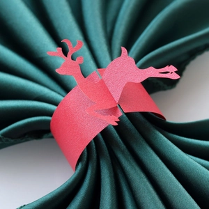 Macro detail of a red reindeer paper napkin ring on a dark green satin cloth napkin
