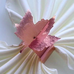 Detailed macro of rose gold maple leaf napkin ring with delicate hollow dot patterns