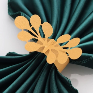 Elegant gold laser-cut paper napkin ring with floral patterns on a dark green satin napkin
