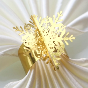 Macro view of a laser-cut gold snowflake napkin ring on a white satin cloth