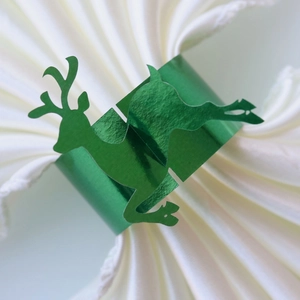Detail of a shiny metallic green reindeer paper napkin ring on a white pleated napkin