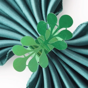 Macro detail of laser-cut green glitter napkin ring with floral pattern on satin cloth