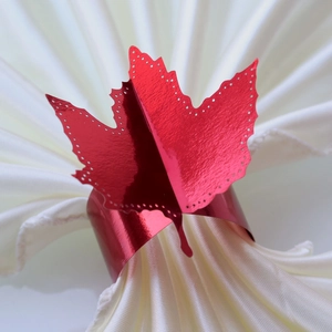 Macro detail of red metallic maple leaf napkin ring with intricate cutout edge on white fabric