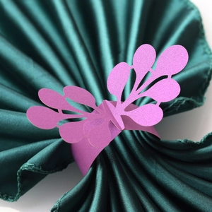 Macro view of purple laser-cut paper napkin ring with floral lace design on green satin