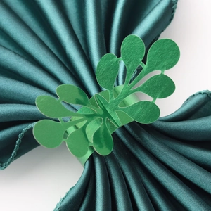 Close-up of sparkling green hollowed-out leaf napkin rings on dark satin fabric