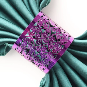 Close-up of purple hollow floral napkin ring on a dark green satin fabric table setting