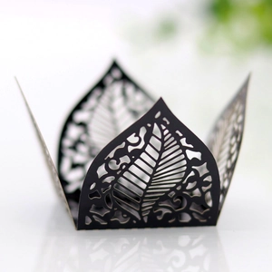 Macro detail of laser-cut black paper cupcake wrapper with intricate leaf patterns