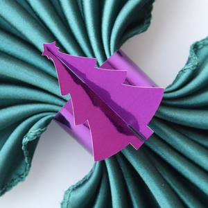 Détail d'un rond de serviette sapin de Noël violet métallique sur satin vert