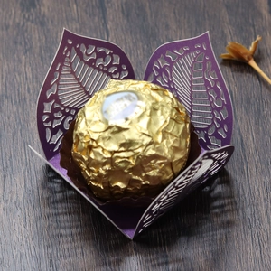 Macro shot of purple laser-cut leaf candy box with a chocolate on wood background