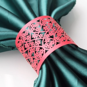 Close-up of red laser-cut paper napkin ring with intricate floral pattern on green satin