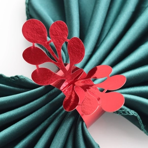 Close-up of red mirror finish napkin ring with hollow leaf design on green silk cloth