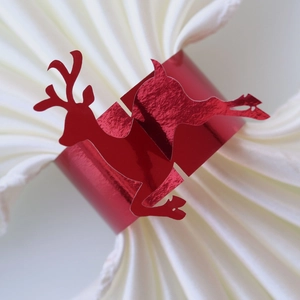 Detail of a shiny red reindeer paper napkin ring on a white napkin for Christmas decor