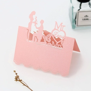 Macro detail of pink glitter laser-cut wedding place card with Mr Love Mrs heart design
