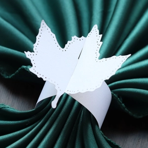 Close-up of a white laser-cut maple leaf paper napkin ring on a green satin cloth