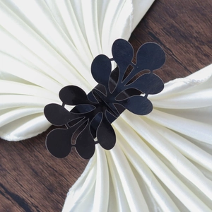 Macro shot of black laser-cut floral napkin ring on white pleated fabric with leaf patterns