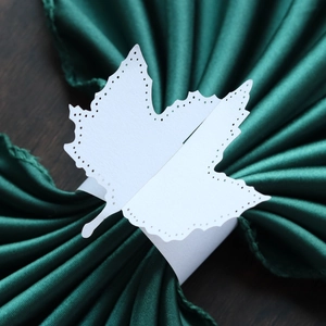 Detailed close-up of white maple leaf paper napkin ring on dark green fabric