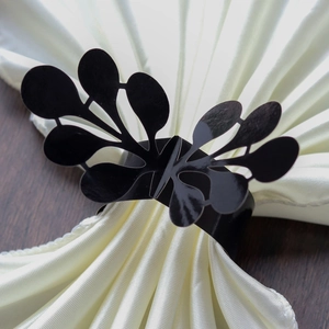 Close-up of black hollow leaf napkin ring on white satin fabric over a wooden table