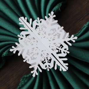 Macro shot of laser-cut white snowflake napkin ring on dark green satin background