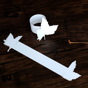Detail of laser-cut white maple leaf paper napkin rings on a dark wooden texture