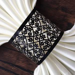 Close-up of black hollow flower napkin ring on a white silk cloth with wooden background