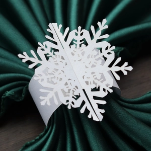 Detail of white laser-cut snowflake paper napkin ring on green silk fabric backdrop